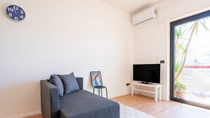 Ein modernes Wohnzimmer mit einer Couch, einem Fernseher auf einem Lowboard, einer Uhr und einem Fenster mit Blick.