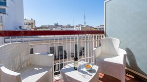 Ein Balkon mit Korbstühlen, einem Tisch mit Flasche und Schüssel, und freiem Blick auf Gebäude im Hintergrund.