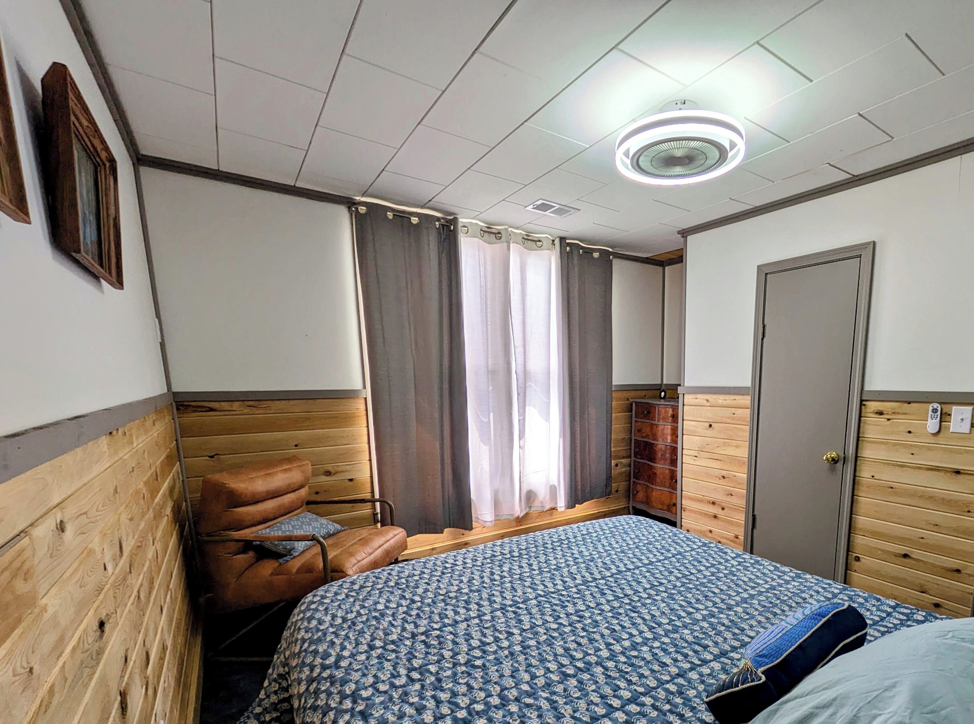 A bedroom with a bed, a wooden chair, a wardrobe, and a window with curtains.