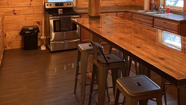 Een houten cabin interieur met een keukenhoek, inclusief een groot houten eiland, barstoelen, een roestvrijstalen fornuis en een spoelbak.