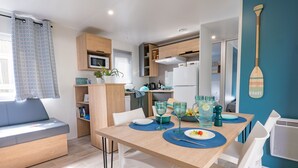 Un espacio habitable compacto con una mesa de comedor, sillas blancas, un sofá y una zona de cocina.