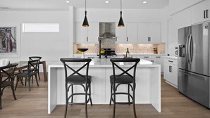 Cozinha moderna com ilha central, eletrodomésticos de aço inoxidável e iluminação pendente.