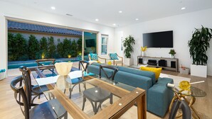 Uma sala de estar moderna com uma mesa de jantar de vidro, sofá azul e uma televisão grande na parede.