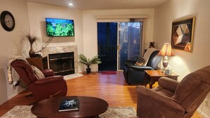 A living room with a fireplace, a television mounted on the wall, and a sliding glass door leading to an outdoor area. - Pools~Screened-In Deck~Dog-Friendly~2 King Beds (Branson)