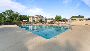 A swimming pool with lounge chairs and umbrellas, surrounded by a fence and trees. - Pools~Screened-In Deck~Dog-Friendly~2 King Beds (Branson)