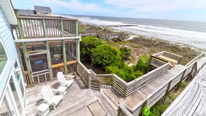 A wooden deck with white chairs, a glass-enclosed room, and a view of the ocean. - El Mar! Beachfront - Every room is oceanfront with it's own porch & bathroom access! (Folly Beach)