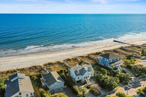 Une propriété située sur la côte, avec vue sur la plage, comprenant une grande maison dotée d’un balcon et une maison plus petite à proximité.