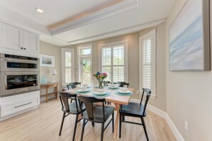 A modern kitchen with white cabinetry, a stainless steel oven, and a dining area with a wooden table and black chairs. - Once Upon A Tide managed by Beach Retreats FL Anna Maria Island (Anna Maria)