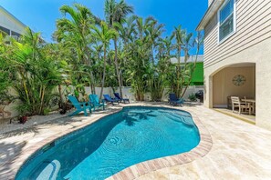 A swimming pool with lounge chairs, surrounded by palm trees and a patio area. - Once Upon A Tide managed by Beach Retreats FL Anna Maria Island (Anna Maria)