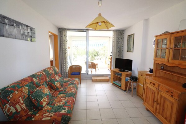 Un salon comprenant un canapé, un téléviseur, un meuble en bois et une porte-fenêtre coulissante donnant sur un balcon.