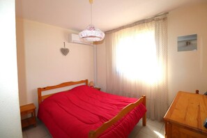 Une chambre à coucher avec un lit en bois, une table de chevet, une lampe, un radiateur fixé au mur et une fenêtre avec des rideaux.