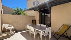 Un patio al aire libre con mesa y sillas, un espacio cubierto y una puerta corrediza.