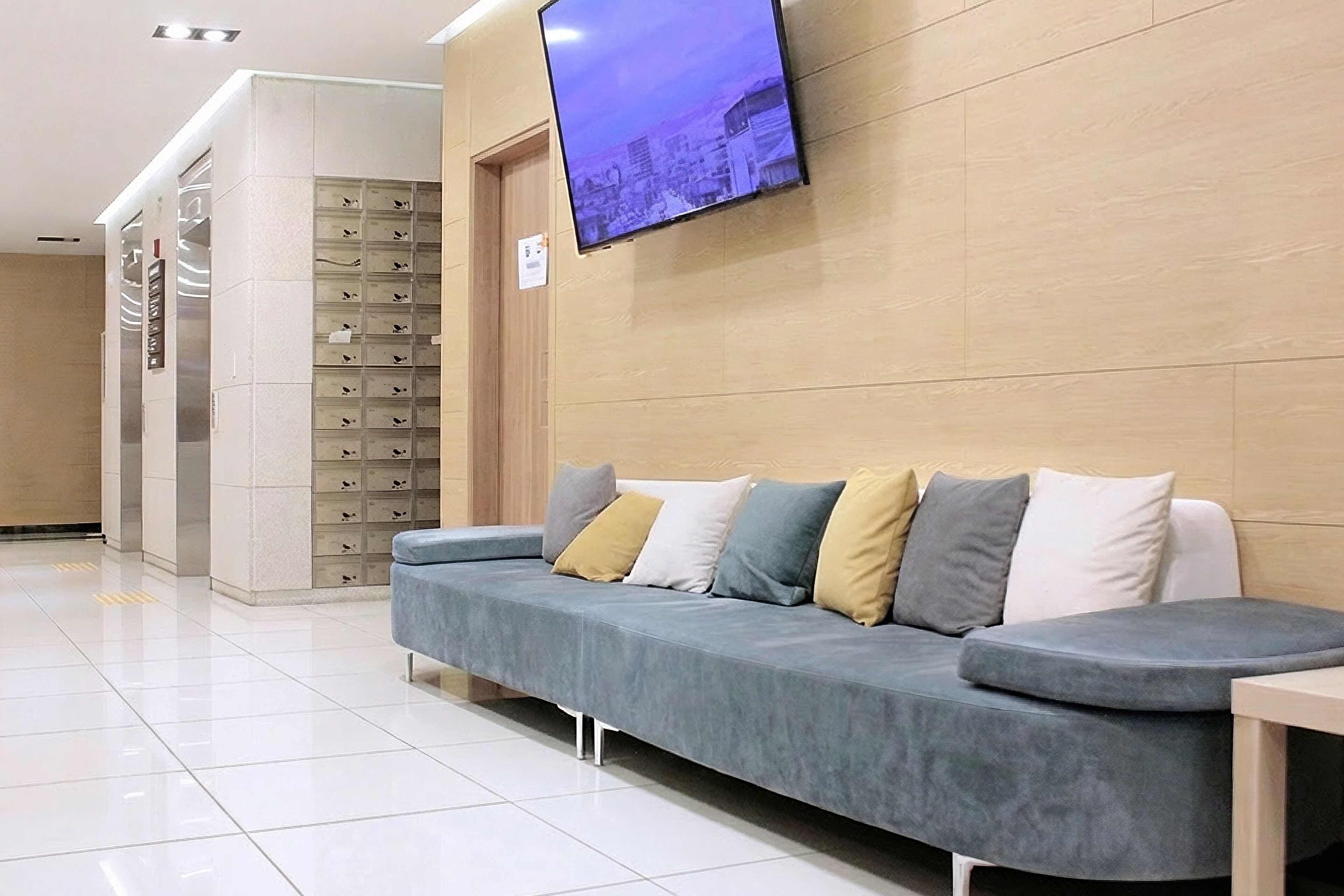A modern waiting area with a grey sofa, a television mounted on the wall, and a shoe storage unit.
