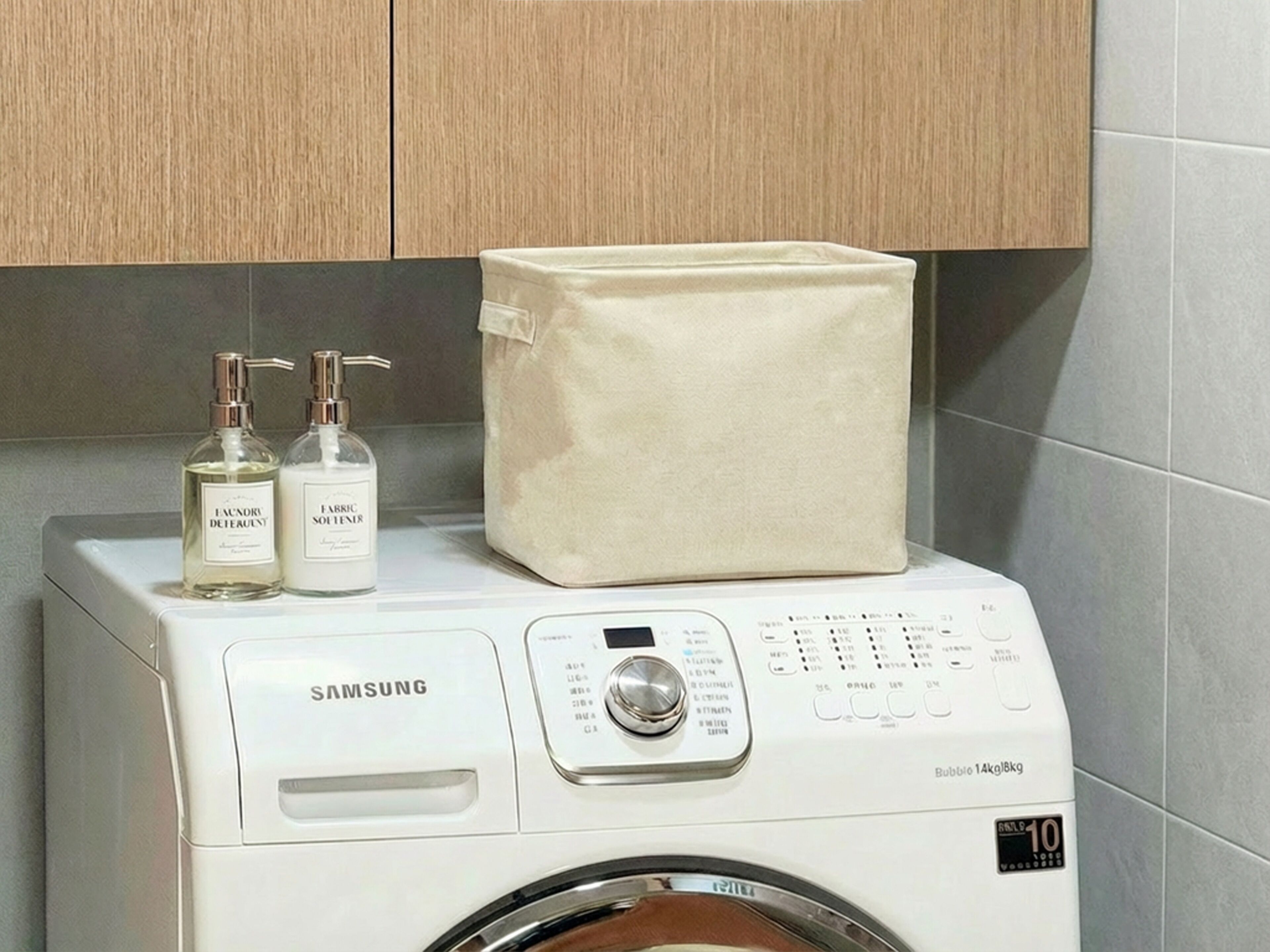 Una lavadora Samsung con pantalla digital, dos botellas de detergente para la ropa y una bolsa beige para la colada encima.
