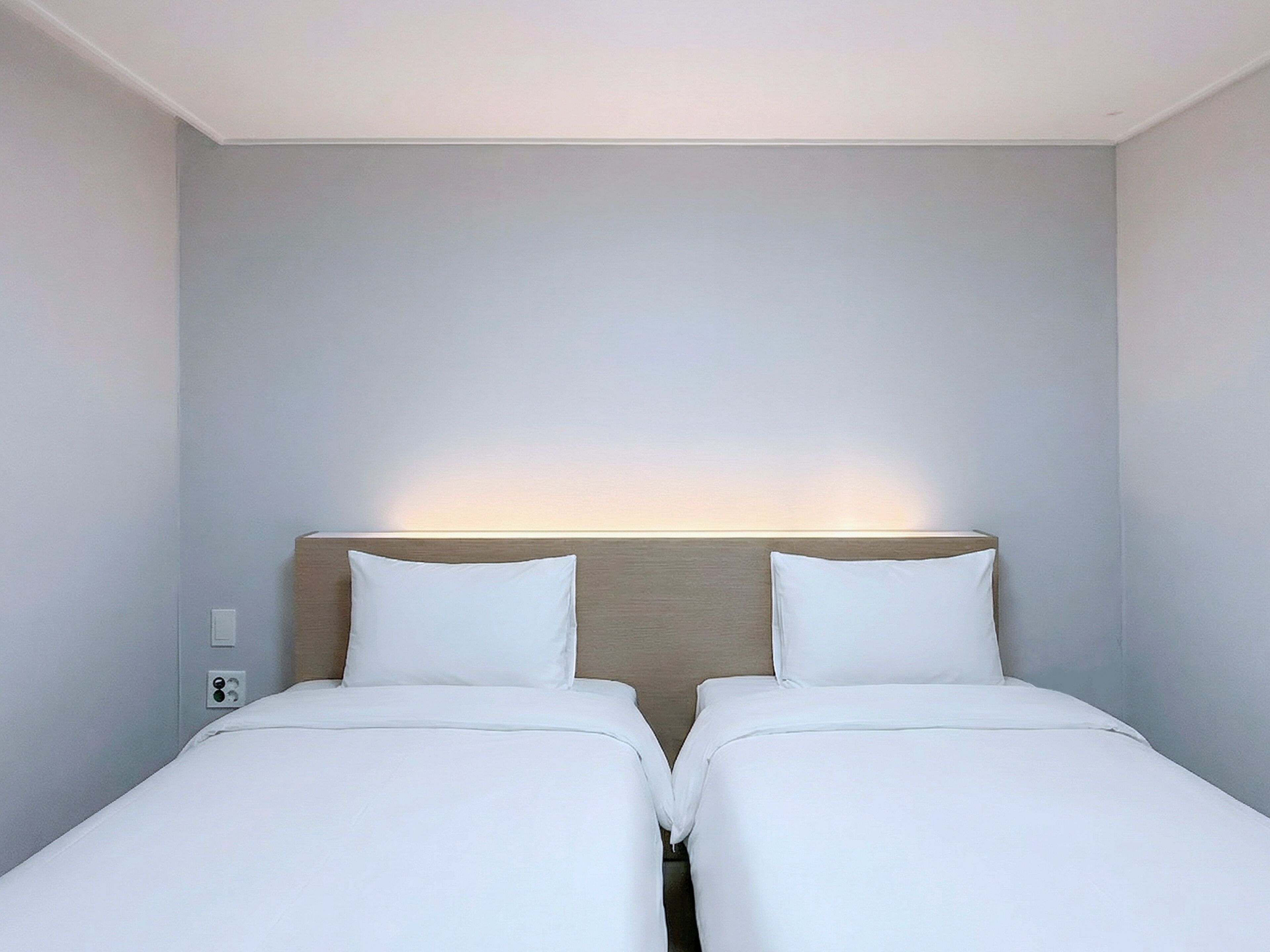 A hotel room with two single beds, a wooden headboard, and a wall-mounted light.
