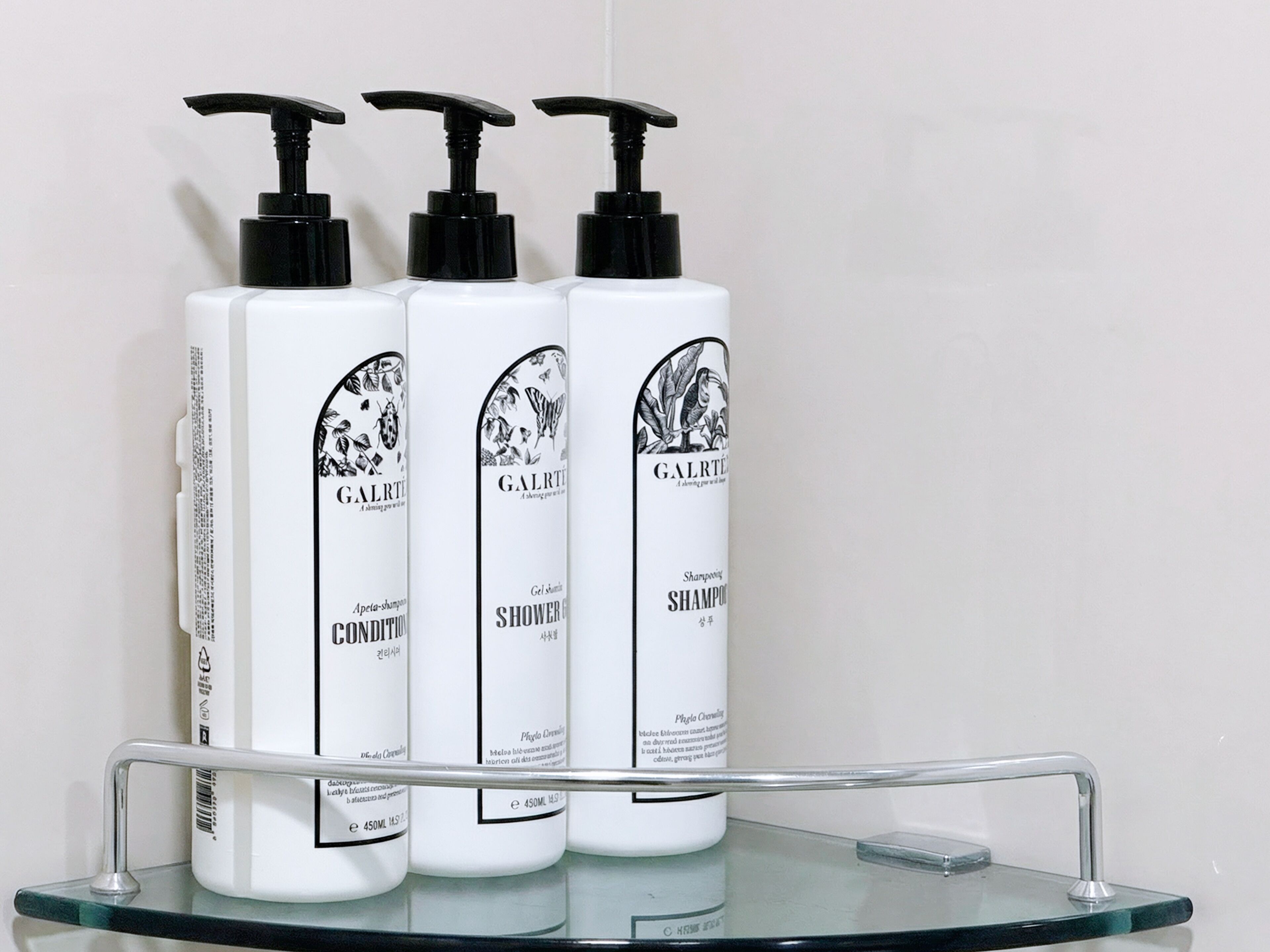 Three bottles of Galrti shower gel on a glass shelf.