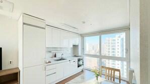 Una cocina moderna con armarios blancos, encimera de mármol y vistas a rascacielos a través de amplios ventanales.