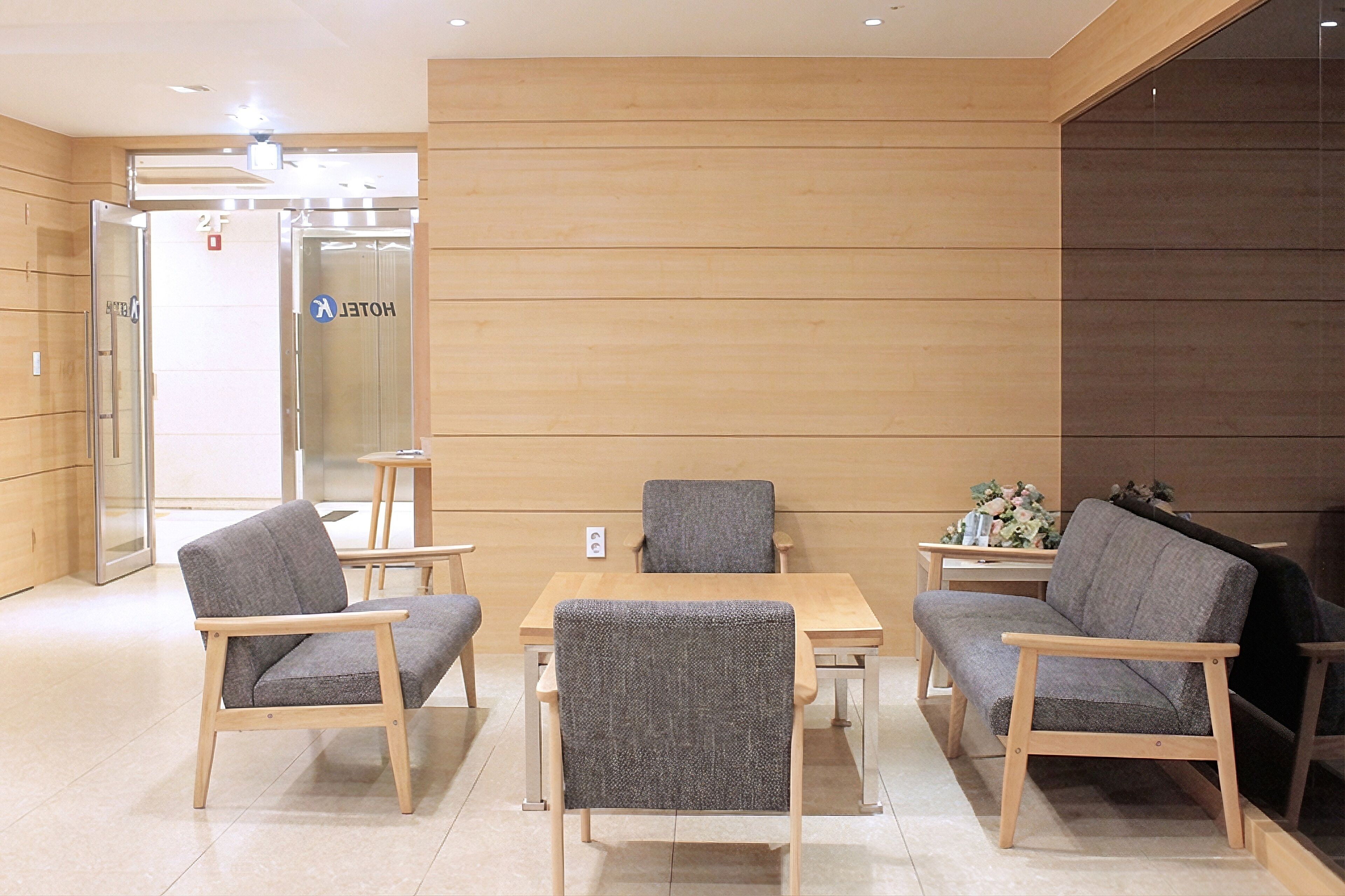 A hotel lobby with wooden panel walls, a reception desk, and seating arrangements including a table and chairs.