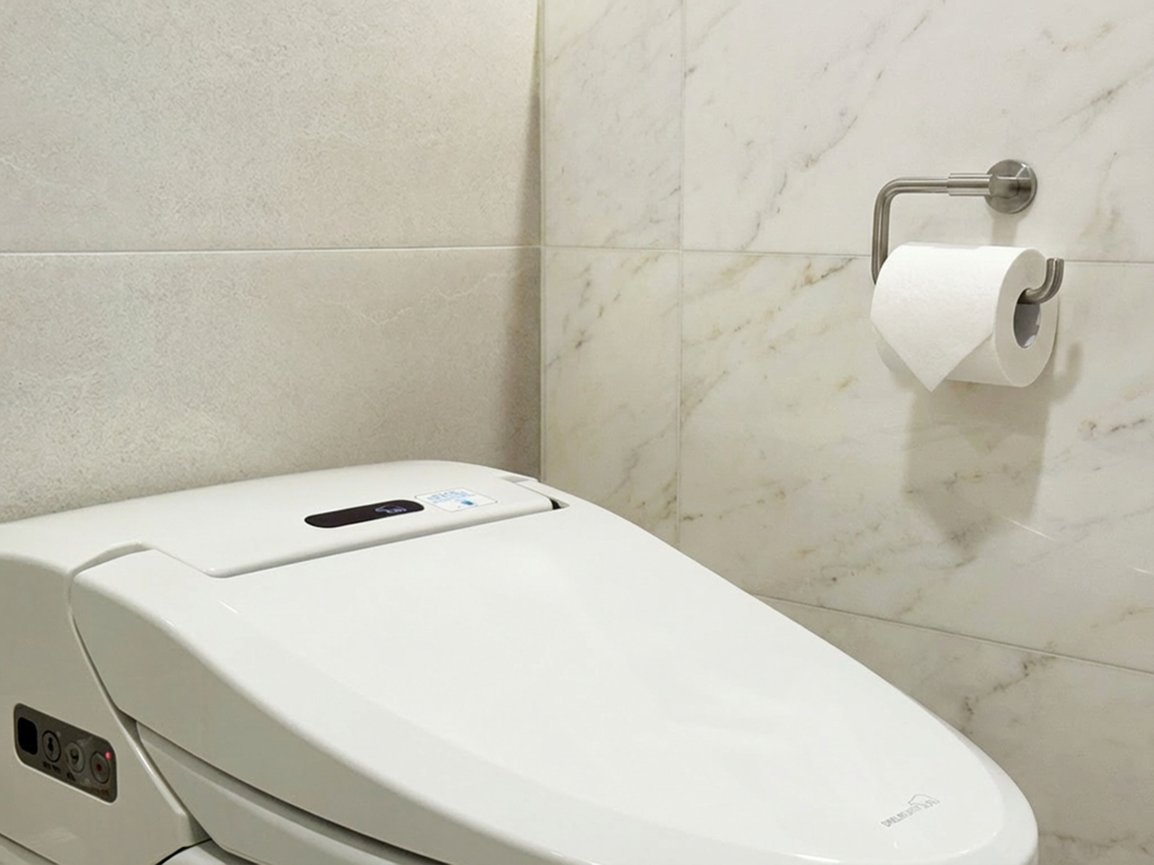 A modern toilet with a digital interface, a toilet paper holder, and a marble-tiled wall.