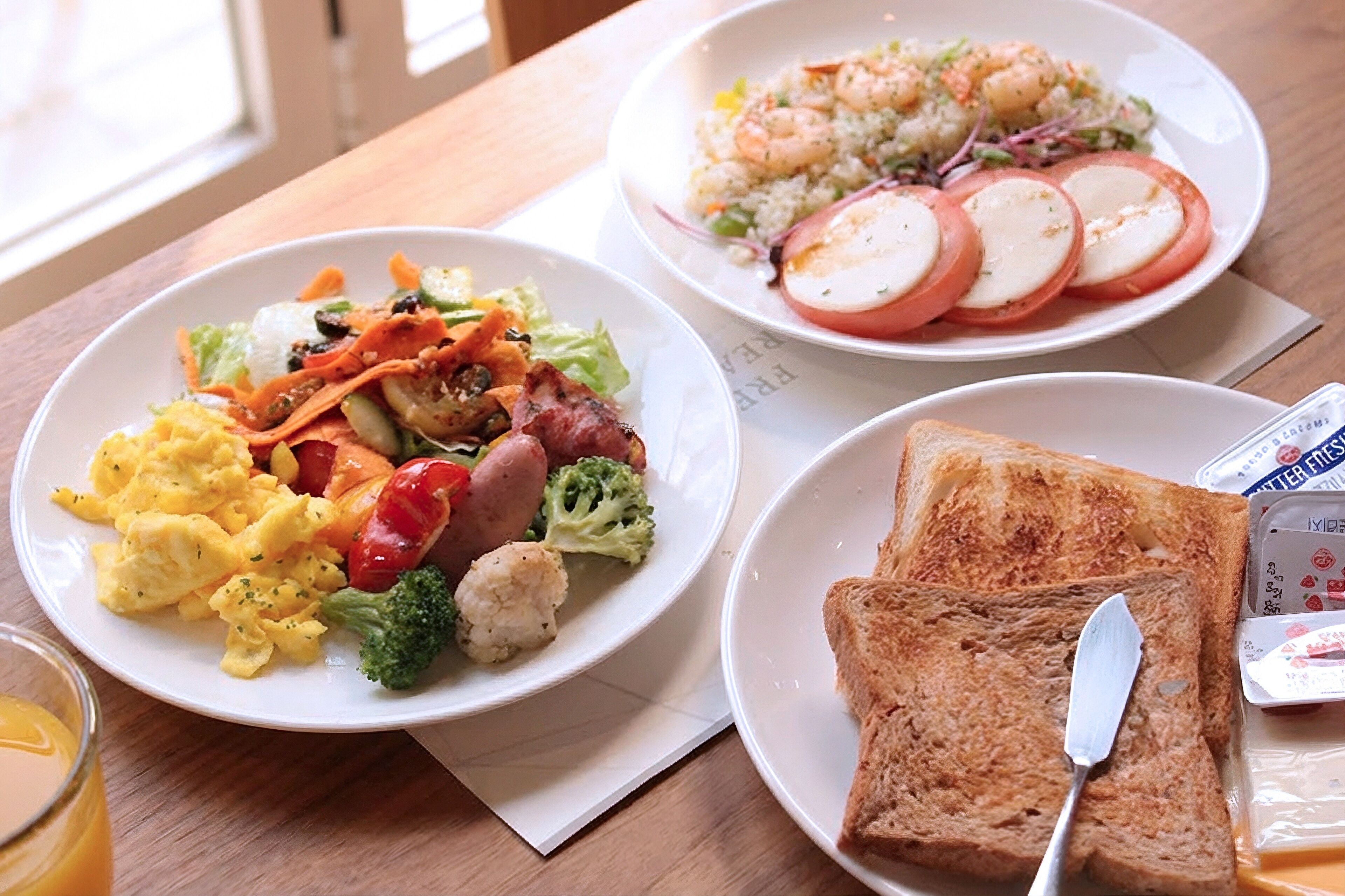 A table with three plates of food, including scrambled eggs, vegetables, and toast.