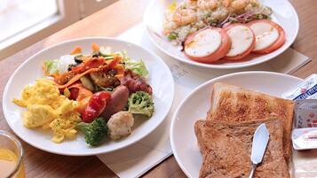 Una mesa con tres platos de comida, entre ellos huevos revueltos, verduras y tostadas.