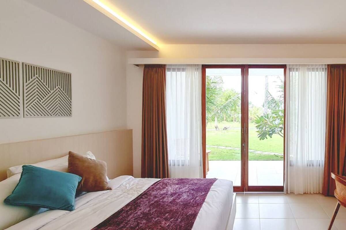A hotel room with a bed, a desk, and a view of a garden through a sliding door.