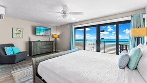 Un dormitorio con una cama grande, ventilador de techo, televisión, cómoda y vista al océano.