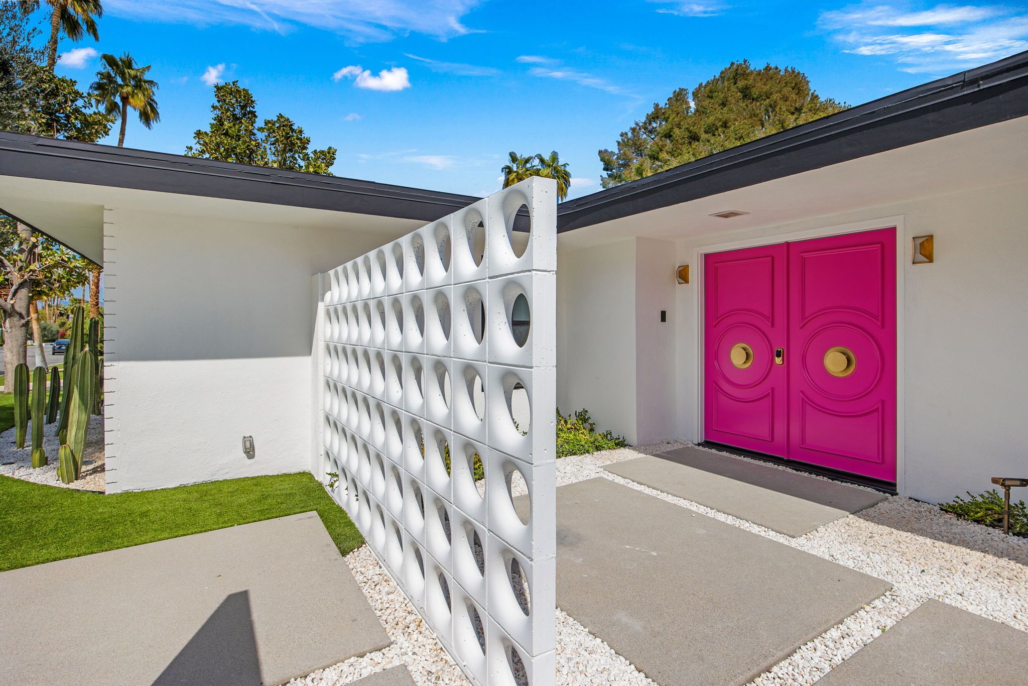 A modern house with a white exterior, a pink double door, and a white fence with circular cutouts.