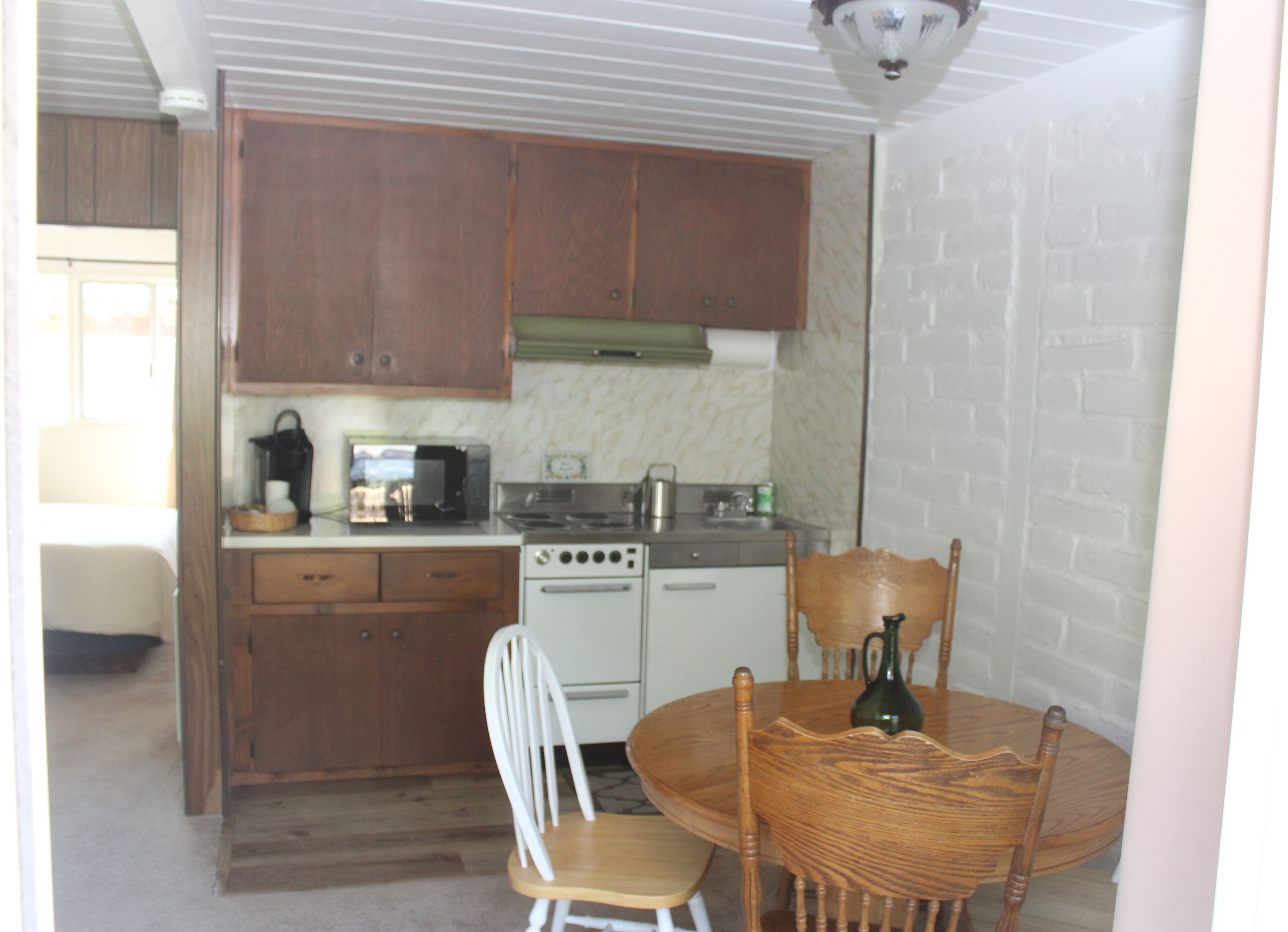 A compact kitchen with wooden cabinets, a stove, a microwave, and a dining area with a table and chairs.