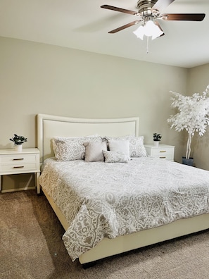 Une chambre à coucher avec un lit, des tables de chevet, un ventilateur de plafond et une plante en pot.