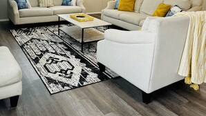 Un salon avec deux canapés, une table basse, un tapis à motifs et un ventilateur de plafond.
