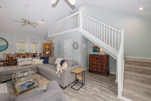 Relax in this inviting living area with a high ceiling, comfortable sofa, and wooden staircase.
