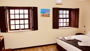 A bedroom with two windows, a bed, a bedside table, and a wall-mounted lamp. - Quiet, Comfortable & Amazing Location (Óbidos)