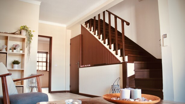 A wooden dining table with candles, a chair, and a staircase with wooden railings. - Quiet, Comfortable & Amazing Location (Óbidos)
