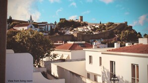 A view from a living room overlooking a historic town with a prominent castle on a hill, surrounded by residential buildings. - Quiet, Comfortable & Amazing Location (Óbidos)