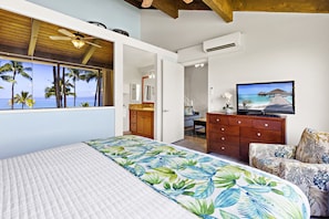 A bedroom with a bed, a television, a dresser, and a view of palm trees and the ocean.