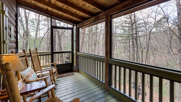 A wooden deck with a view of a forest. There are wooden chairs and a table with a lamp. - Private Hot Tub! ‘Cherry Beary Den’ in Blue Ridge (Blue Ridge)