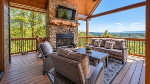 Eine überdachte Terrasse mit Kamin aus Stein, Sitzgelegenheiten im Freien und Blick auf die umliegende Landschaft.