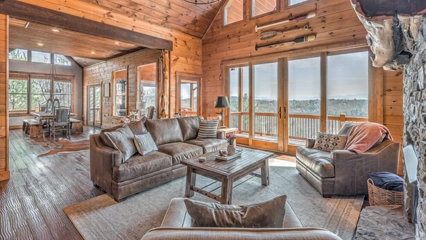 A spacious log cabin interior with a large living area, multiple seating options, and a scenic view through the expansive windows. - Branch Oak Manor - Million Dollar Views | Hot Tub | Fire Pit (Mineral Bluff)