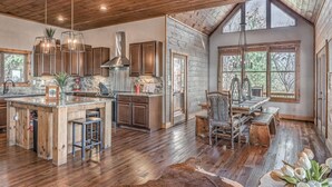 A spacious kitchen with wooden cabinets, a large island, and a dining area with rustic furniture. - Branch Oak Manor - Million Dollar Views | Hot Tub | Fire Pit (Mineral Bluff)
