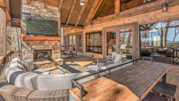 A cozy cabin interior with a stone fireplace, comfortable seating, and large windows offering views of the outdoors.