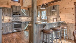 A rustic kitchen with wooden cabinets, a stone backsplash, and a bar area with stools.