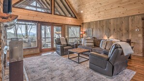 A cozy living room with a fireplace, comfortable seating, and large windows offering a view of the outdoors.