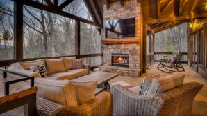 A cozy outdoor living area with a stone fireplace, comfortable seating, and a TV mounted on the wall.