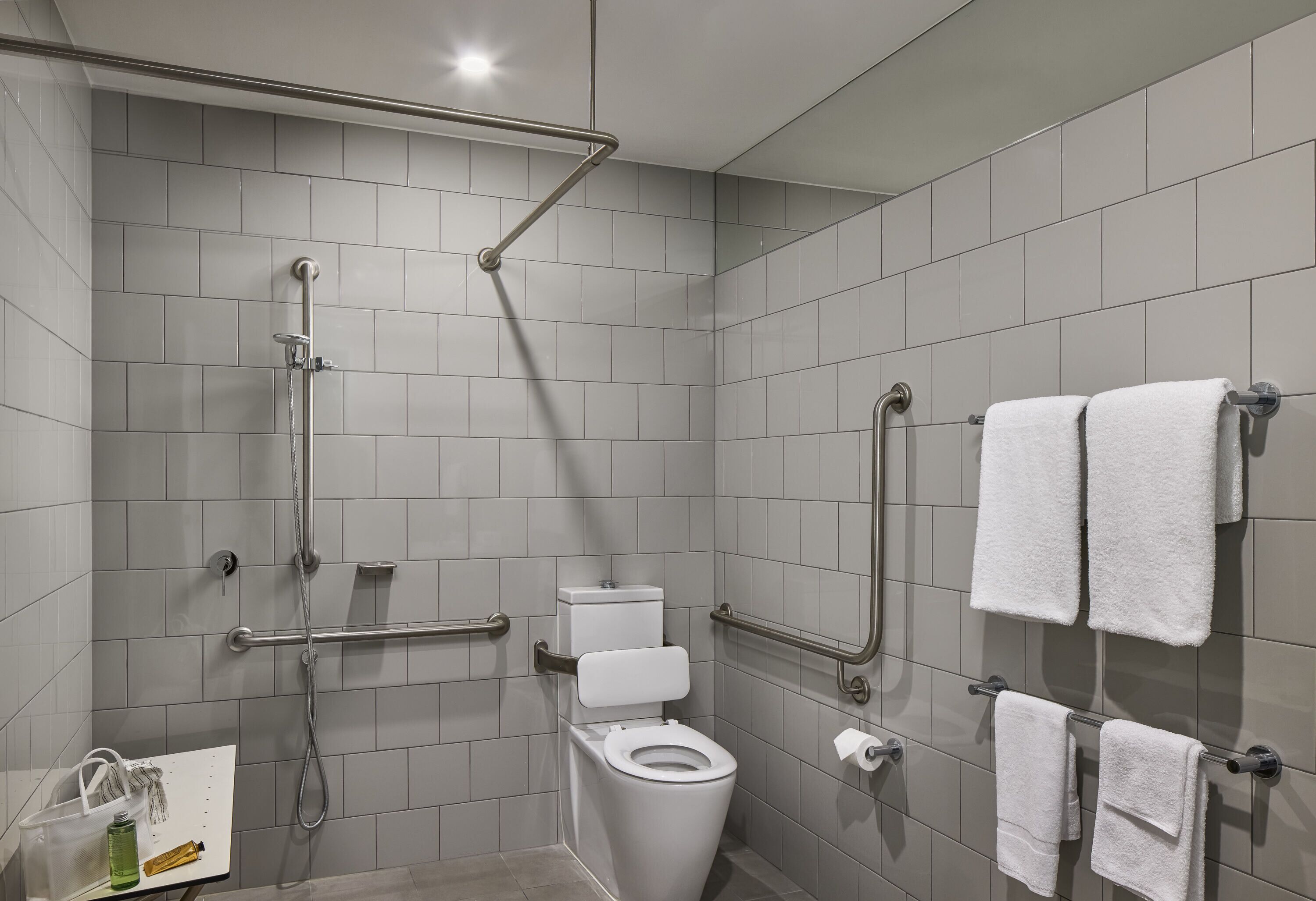 Un baño moderno con inodoro, barras de apoyo, ducha y perchero para toallas.