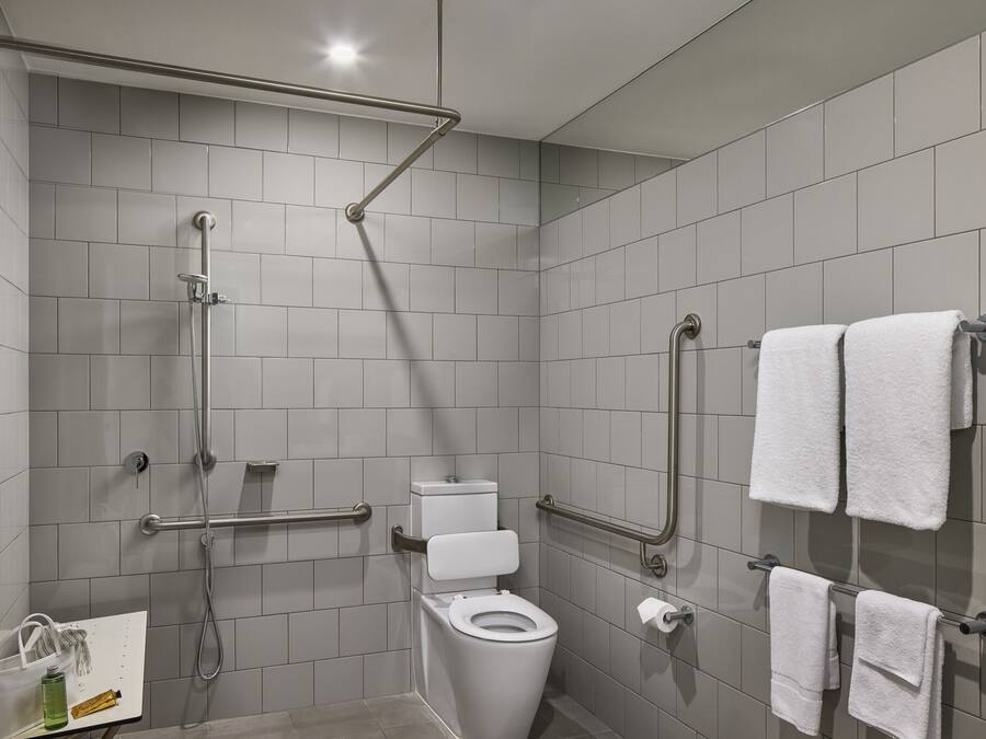 Un baño moderno con inodoro, barras de apoyo, ducha y perchero para toallas.