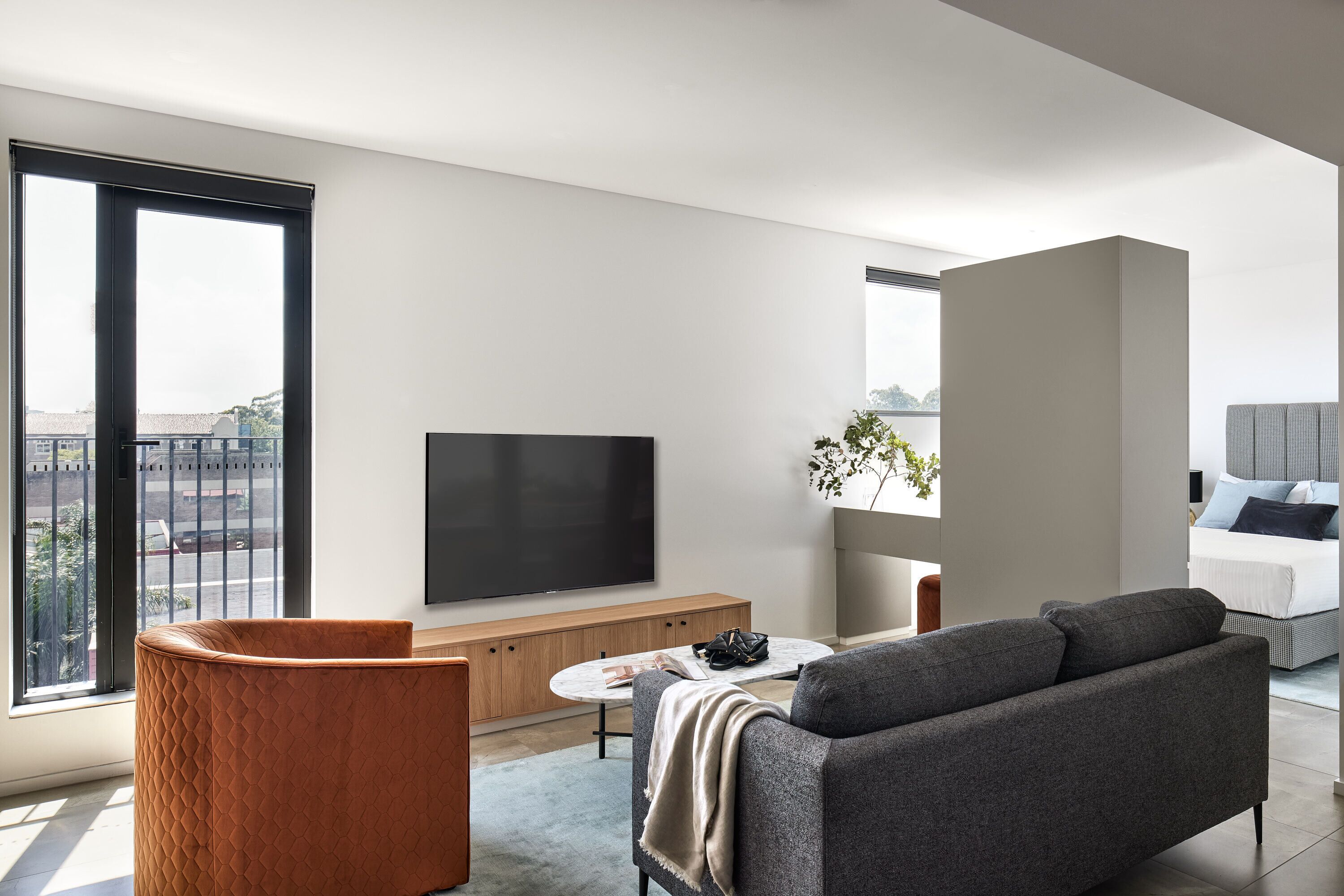 A modern living room with a large TV, a sofa, a coffee table, and a view of the city.