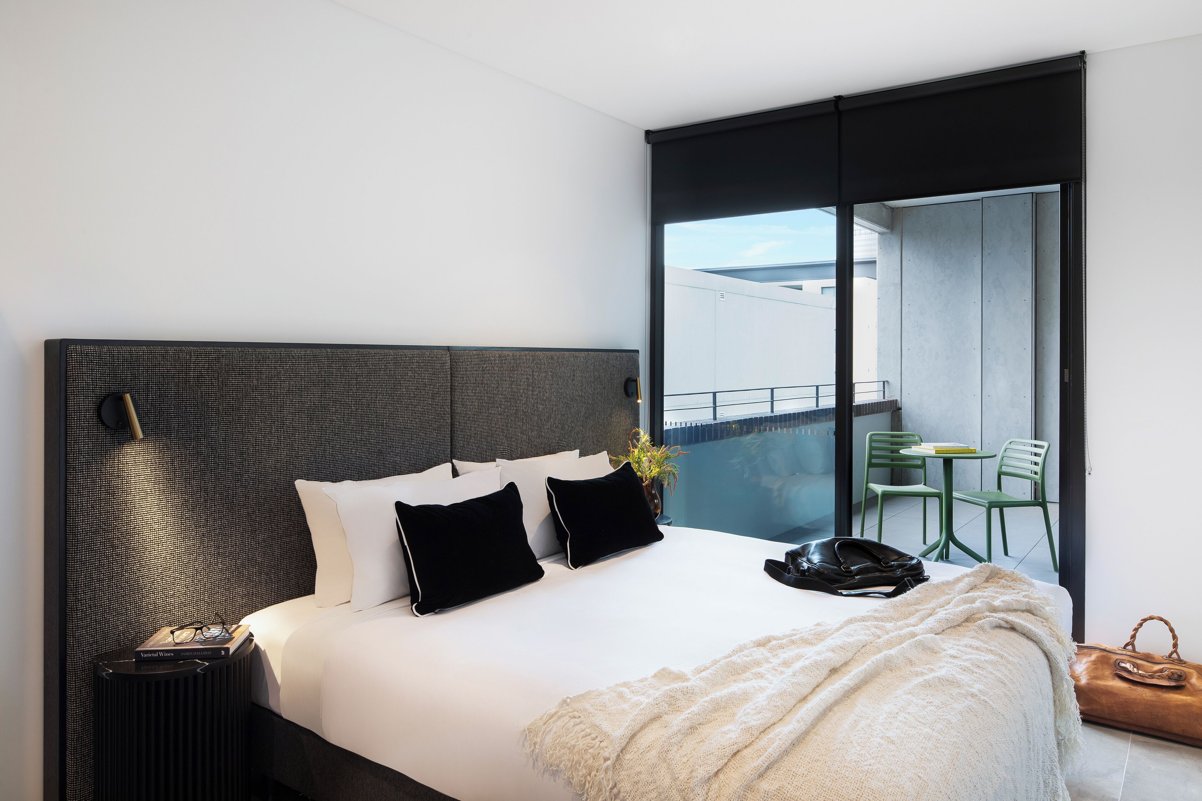 Et moderne hotelværelse med en stor seng, et sengebord, en lampe, udsigt til en balkon og en stol udenfor.