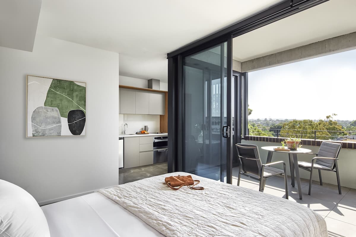 Ein modernes Hotelzimmer mit Bett, Bad, einem Balkon mit Tisch und Stühlen sowie Blick auf die Stadt.
