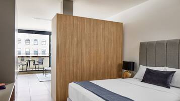 A modern hotel room with a large bed, a wooden partition, a view of the city, and a balcony with outdoor seating.